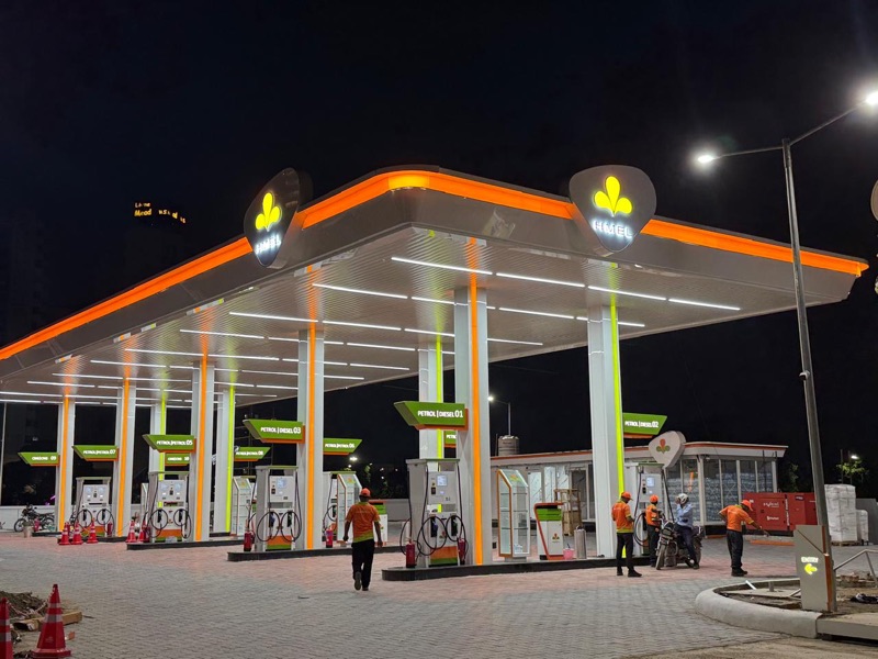 Photograph of a completed fuel station at night with orange-edged canopy and staff on the forecourt